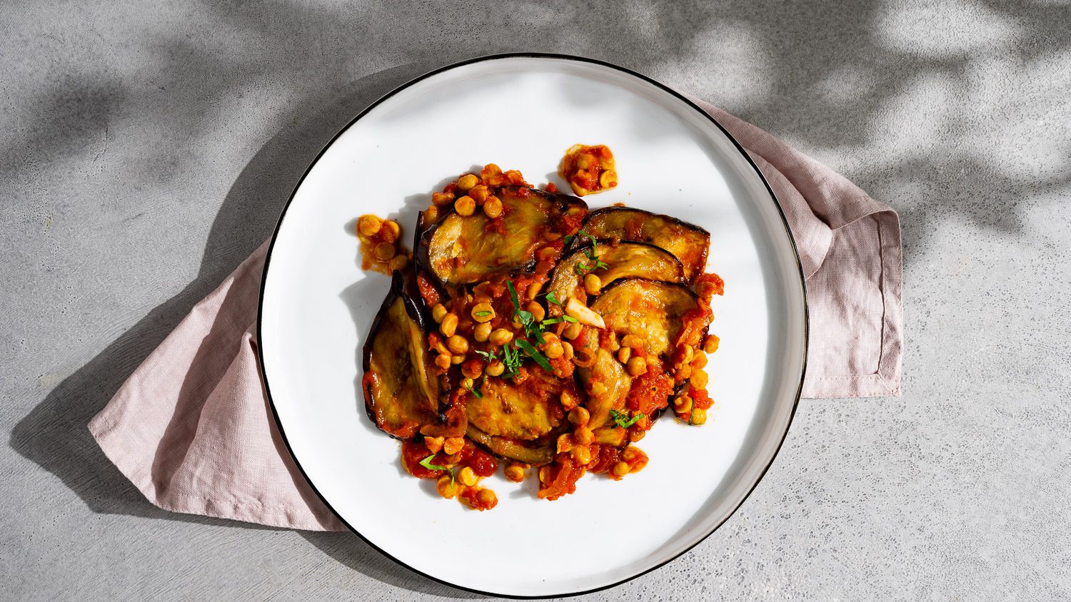 Musakaa frittierte Aubergine in Tomatensauce mit Kichererbsen serviert auf einem weißen teller.