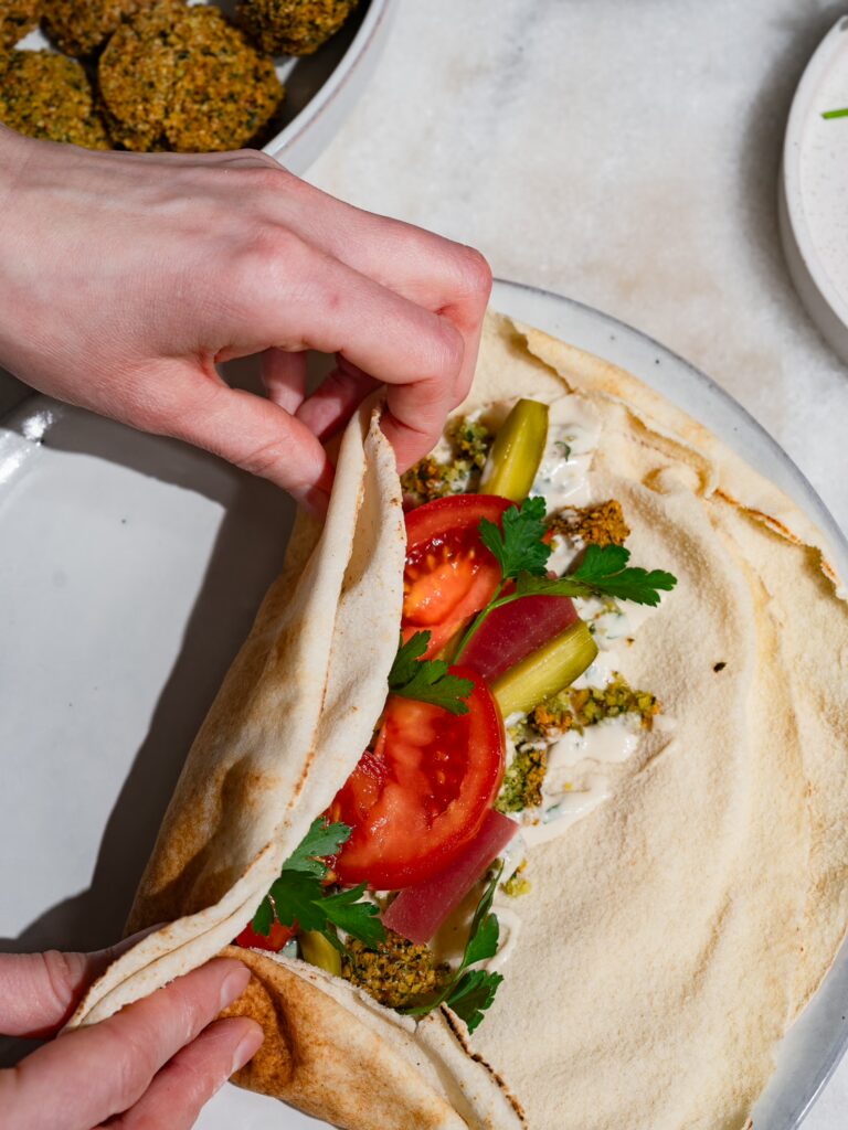 Falafel Wrap wird zum Aufrollen eingeklappt.