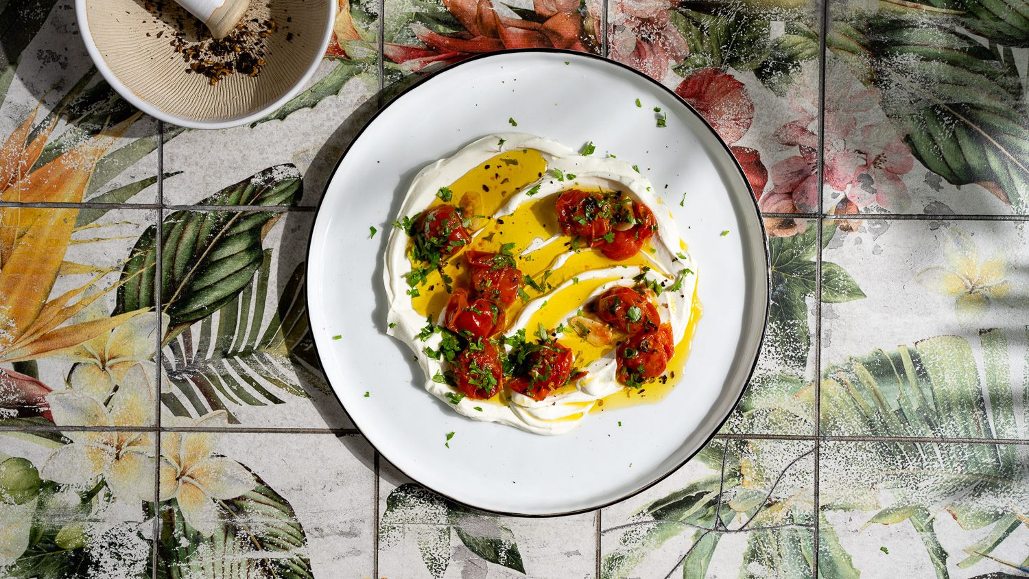 Labneh mit geschmorten Tomaten, Szechuanpfeffer und Koriander auf einem Teller serviert.