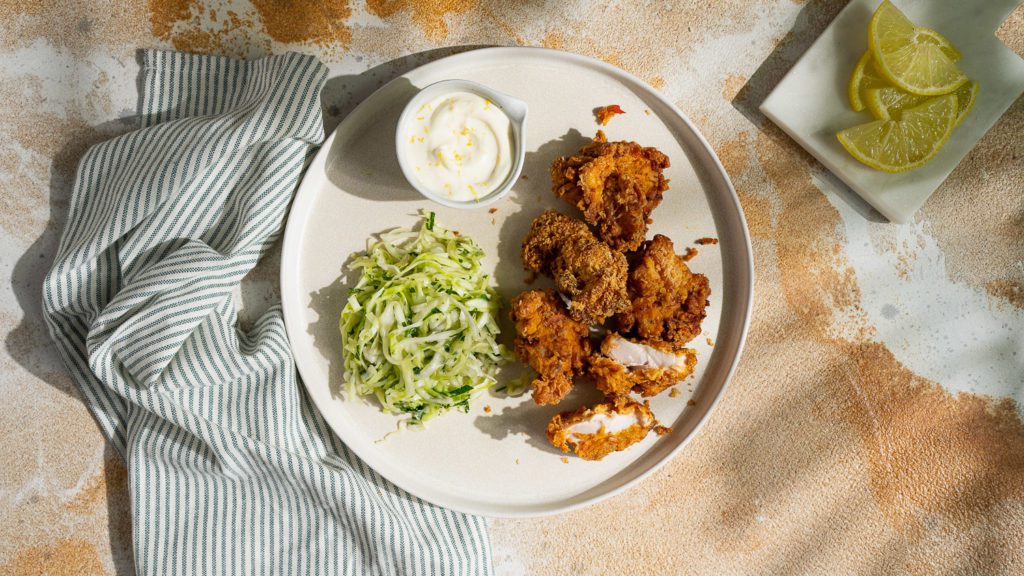 Harissa Fried Chicken auf einem Teller serviert mit Zitronen-Mayonnaise und Coleslaw.