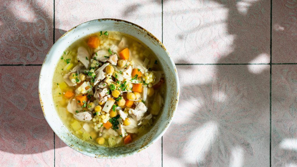 hühnersuppe serviert mit kichererbsen und perlcouscous