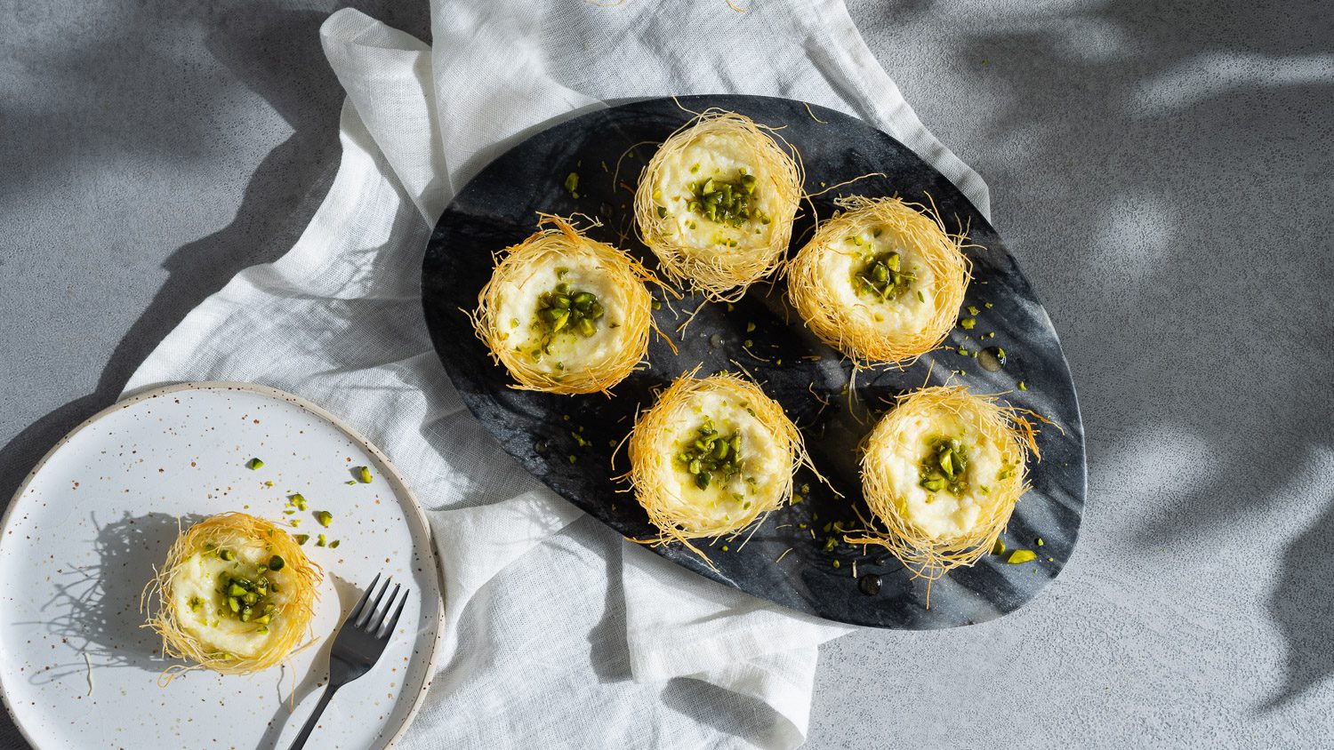 Knefeh Minis mit Pistazien und Honig garniert auf einem dunklen Marmorbrett garniert.