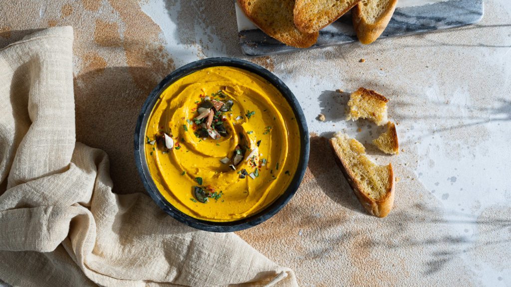 Kürbis-Feta-Dip in einer Schüssel serviert. Daneben liegt geröstetes Brot.