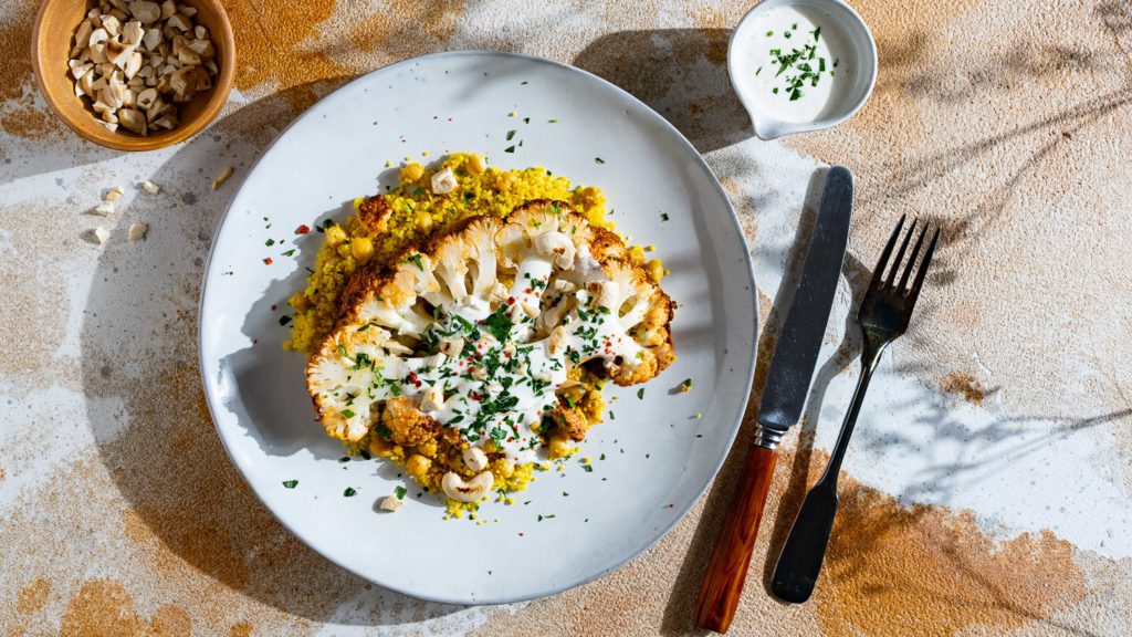 Gerösteter Blumenkohl auf Couscous mit Kichererbsen, serviert mit Tahini-Dip.