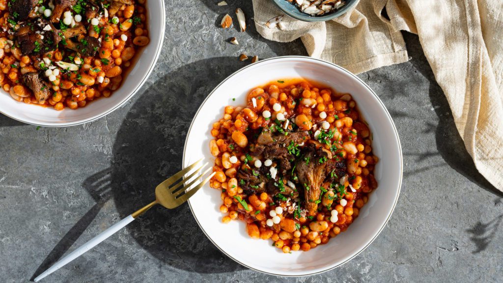 Perlcouscous in tomatensauce mit Pilzen angerichtet auf grauem Untergrund