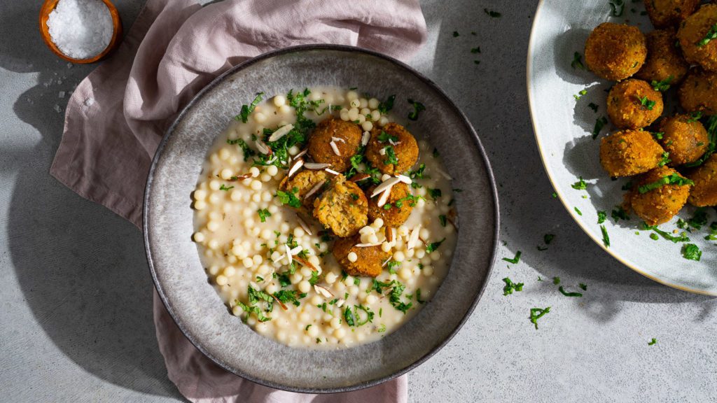 Linsen-Bulgur-Bällchen mit Perlcouscous in Joghurtsauce, serviert in einem tiefen Teller