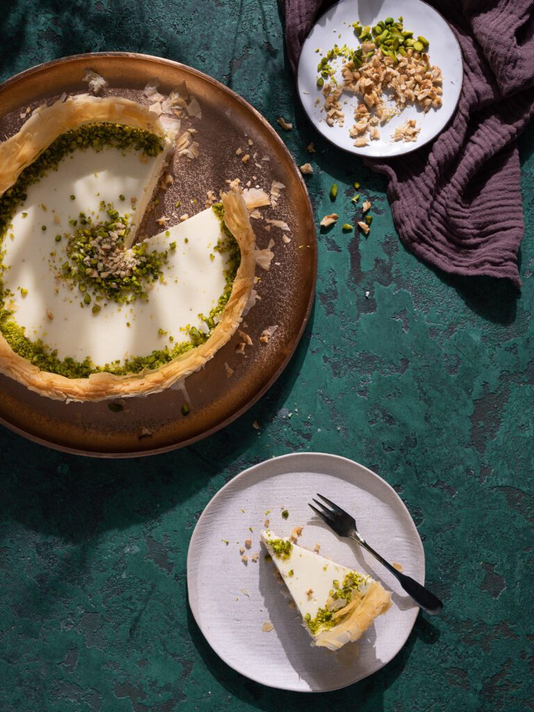 Cheesecake au baklava coupé sur une assiette. À côté, un morceau de gâteau sur une petite assiette.