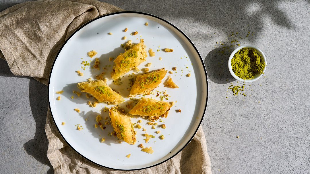 klassisches Baklava angerichtet auf einem weißen Teller auf grauem Untergrund.