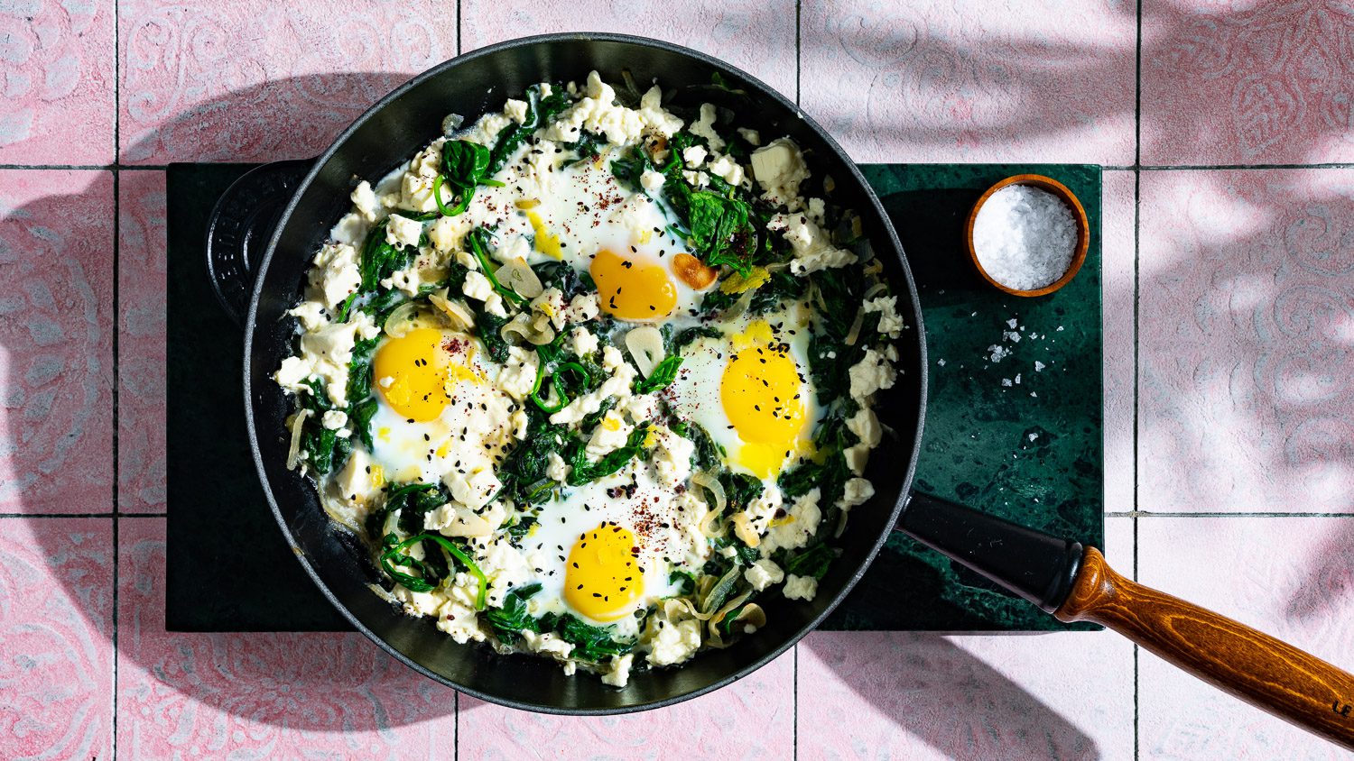 grüne Spinat Shakshuka mit Feta serviert in einer schwarzen Gusspfanne auf grünem Marmorbrett.