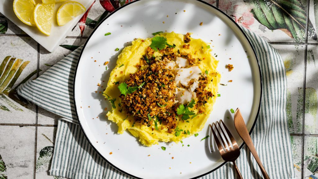 gebackenes kabeljaufilet auf kartoffelstampf serviert auf einem weißen Teller mit Messer und Gabel.