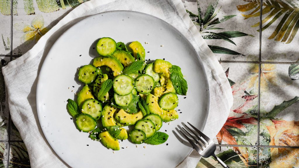 Avocado-Gurken-Salat auf einem hellen Teller serviert. Am Tellerrand liegt eine Gabel.