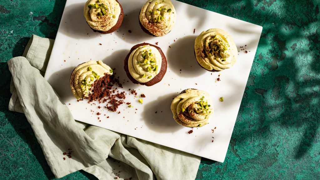 Schokomuffins mit Pistaziencreme stehen auf einem Marmorbrett. Einer von ihnen wurde angebissen.