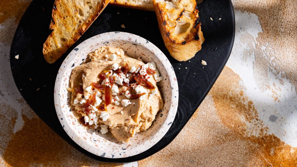 Dattel-Dip mit Frischkäse auf einem Brett serviert. Dazu geröstetes Brot.