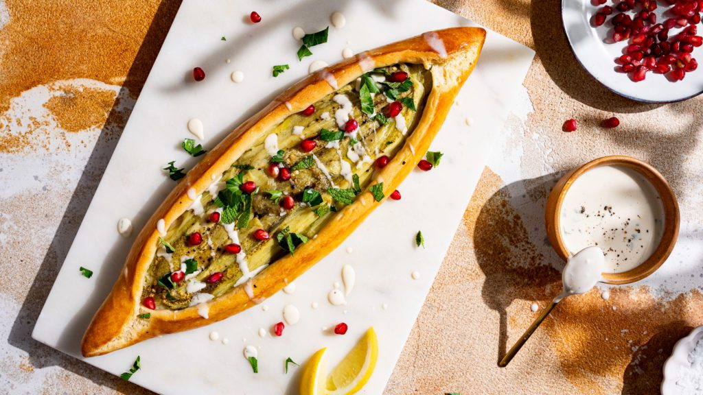 Pide mit Aubergine, serviert mit frischen Kräutern auf einem Marmorbrett.