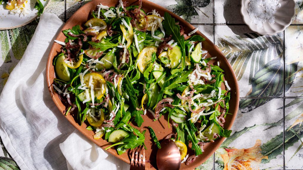 Rucola Salat mit geriebenem Halloumi und Cumin-Zitronen auf einer großen Platte serviert.