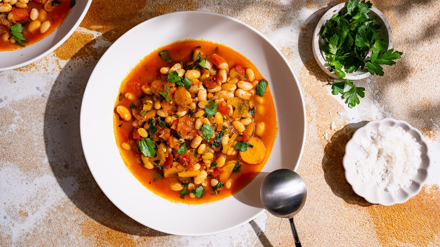 Se colocan sobre una mesa un plato de fasolada y dos pequeños cuencos con perejil y sal.