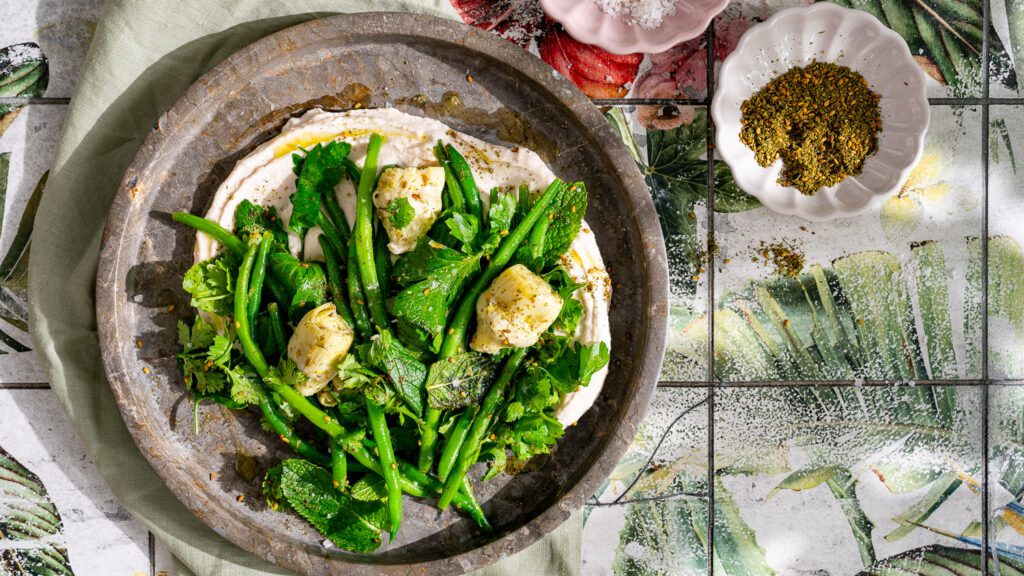 Ensalada de judías verdes con alcachofas y hierbas sobre puré de judías servido en plato.