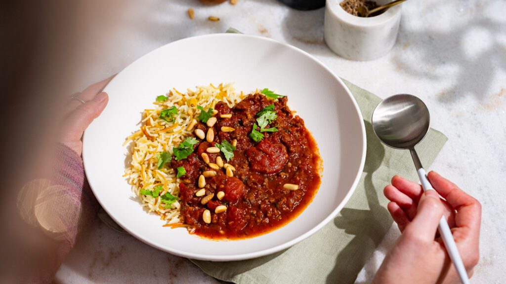 Libanesischer Tomateneintopf mit Hackfleisch, serviert mit Butterreis in einem tiefen Teller.