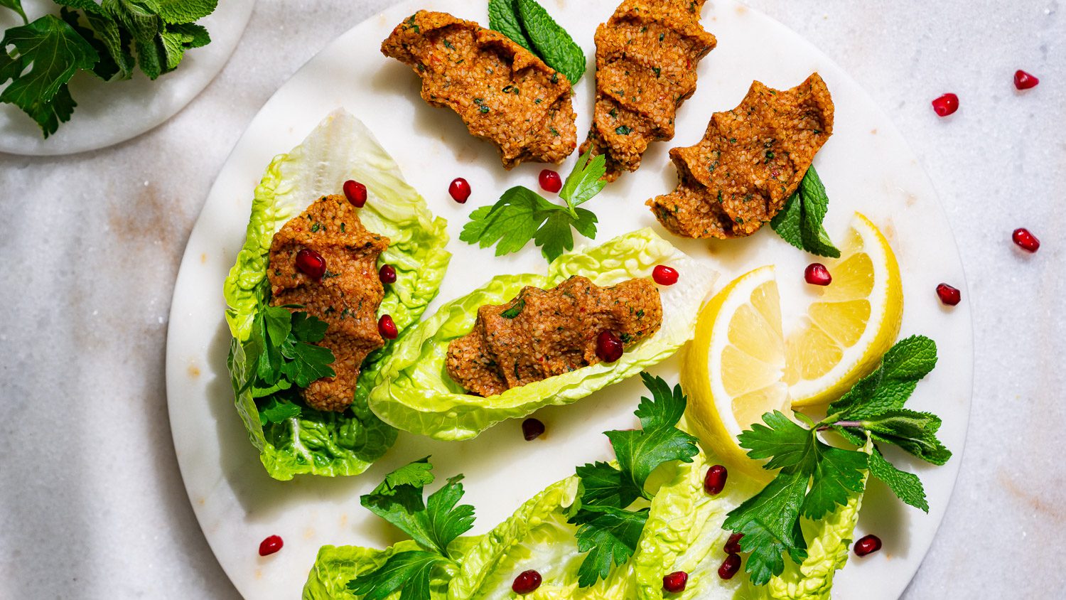 Cigköfte served with salad, herbs, pomegranate seeds and lemons.