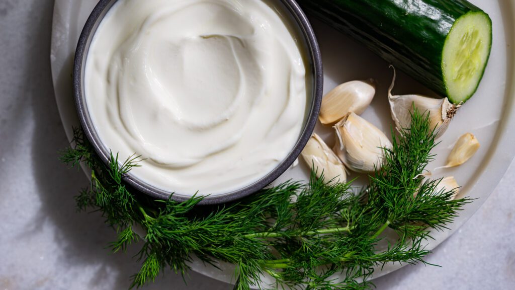 Yogur griego cremoso, eneldo, pepino y dientes de ajo en una fuente.