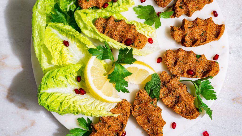 Vegan cigköfte served on a light platter with salad leaves, herbs and pomegranate seeds.