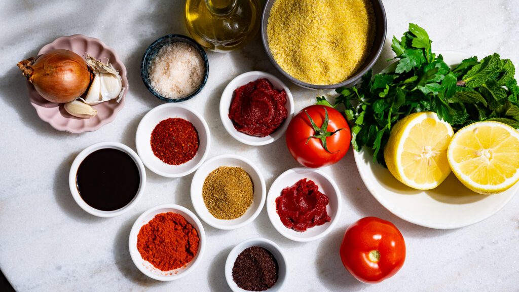 Ingredients for vegan cigköfte are placed in small bowls on a light-colored marble table.