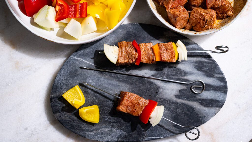Se prepara el shish kebab: Se ensartan en brochetas cebollas, pimientos y carne.