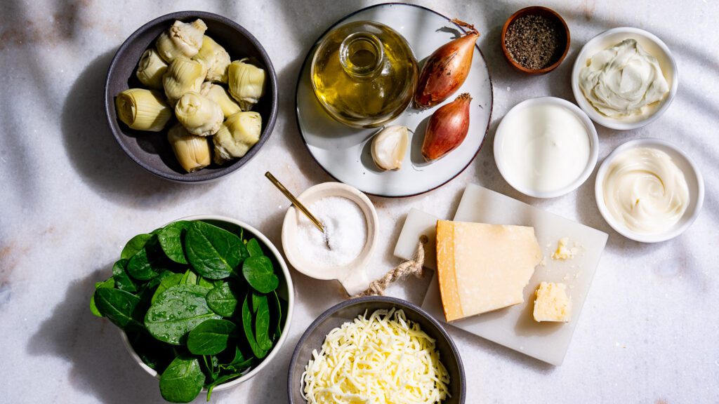 Los ingredientes de la salsa de espinacas y alcachofas se colocan sobre una mesa de mármol claro.