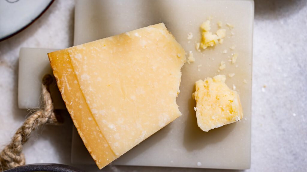Queso parmesano en una tabla de mármol de color claro. Se ha roto un trozo de queso.