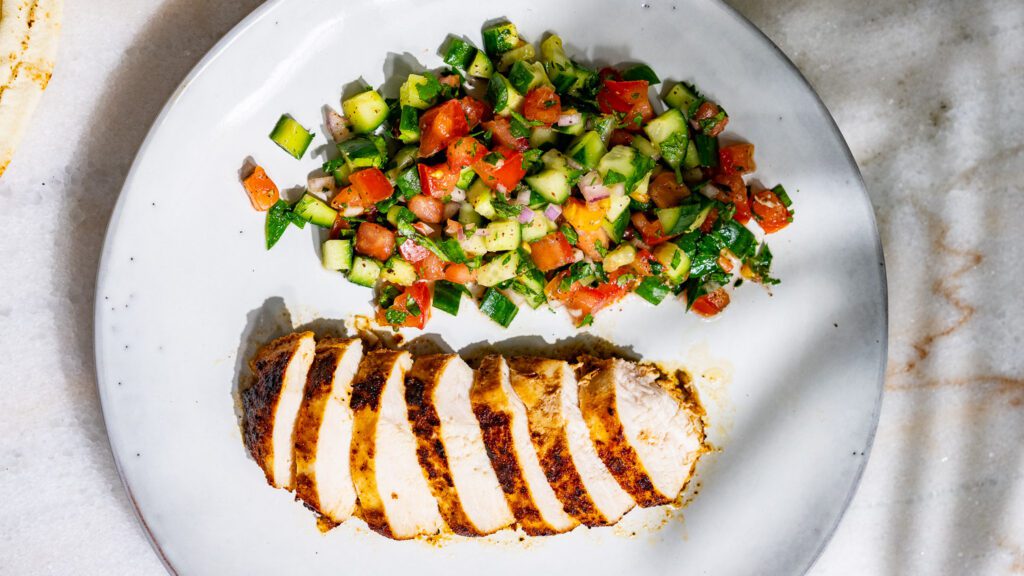 Salade de tomates et de concombres servie dans une assiette avec du blanc de poulet grillé.