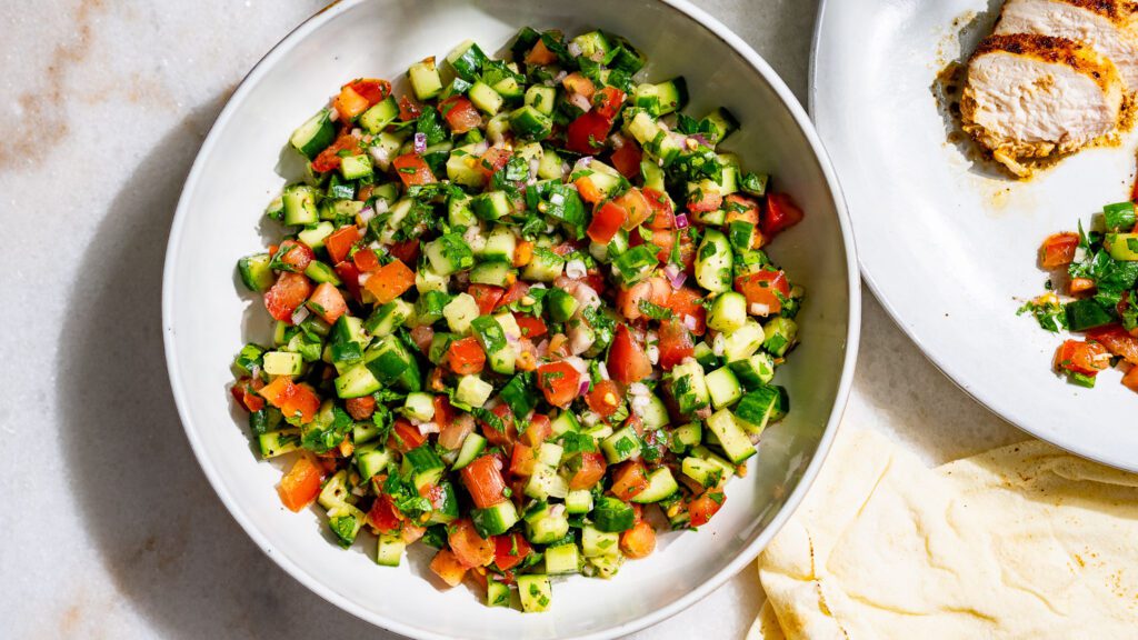 Salade Shirazi servie dans un bol. À côté, il y a une assiette de salade et de poulet.