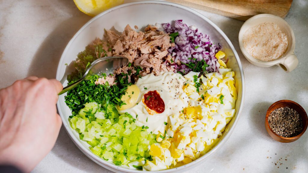 Mezcla todos los ingredientes de la ensalada de atún con una cuchara en un bol.