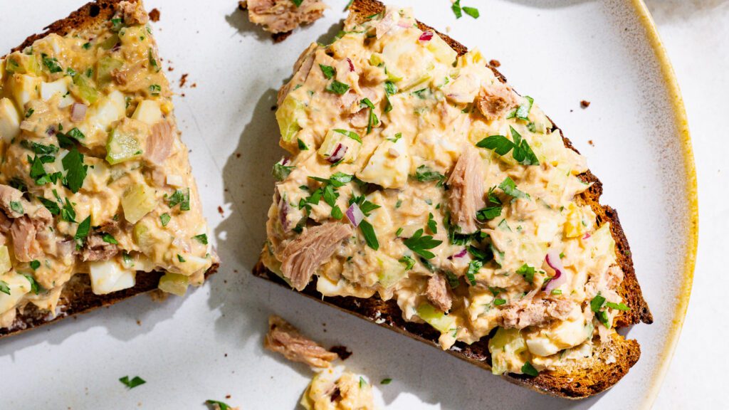 Una rebanada de pan con ensalada de atún cortada por la mitad en un plato.