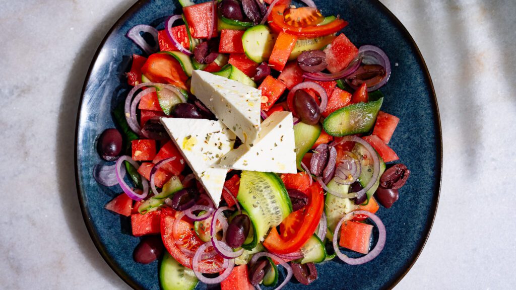 Ensalada griega con sandía servida en un plato de color oscuro.