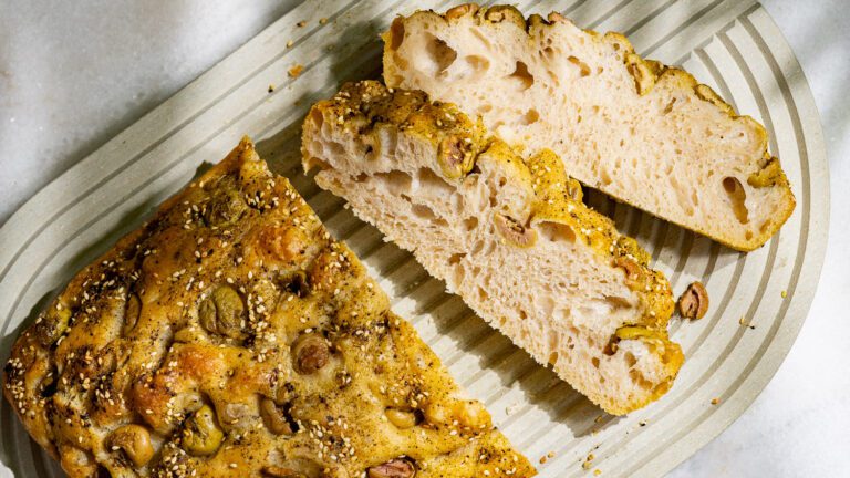 Une focaccia aux olives et au za'atar est découpée sur une planche.