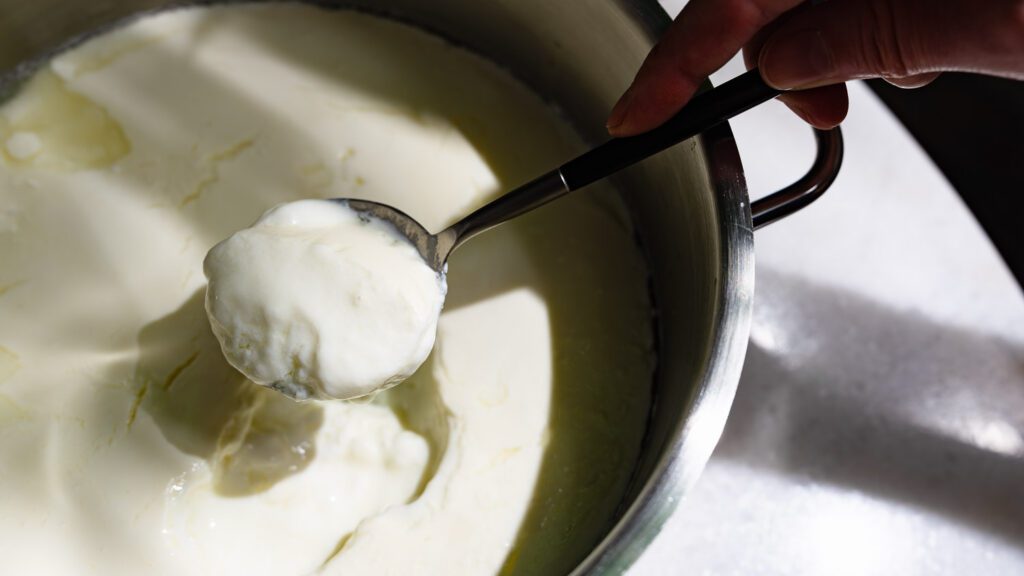 Joghurt selber machen: selbst gemachter Joghurt wird mit einem Löffel aus einem Topf geholt.