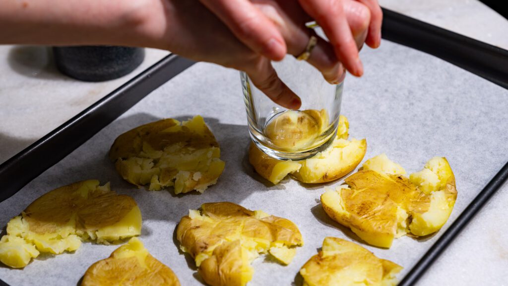 Utiliza un vaso para aplastar las patatas en una bandeja de horno.