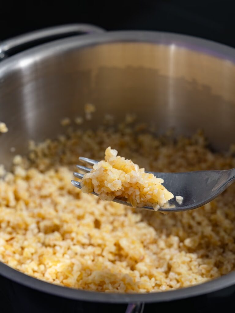 Cooked bulgur on a fork in front of the pot with the rustic cooked bulgur.