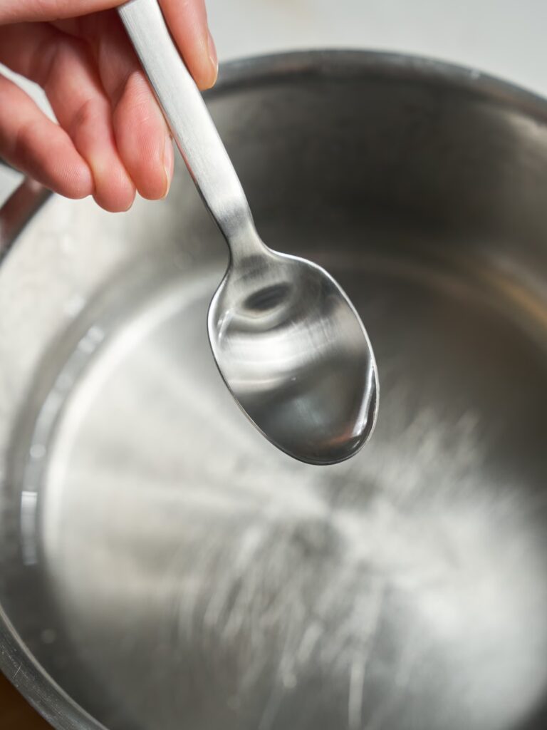 Rosenwasser wird mit einem Löffel in den Zuckersirup für das Baklava mit Pistazien gegeben.