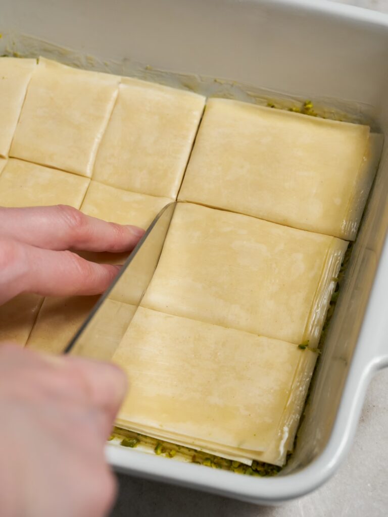 Das Baklava mit Pistazien wird in der Form mit einem Messer geschnitten.