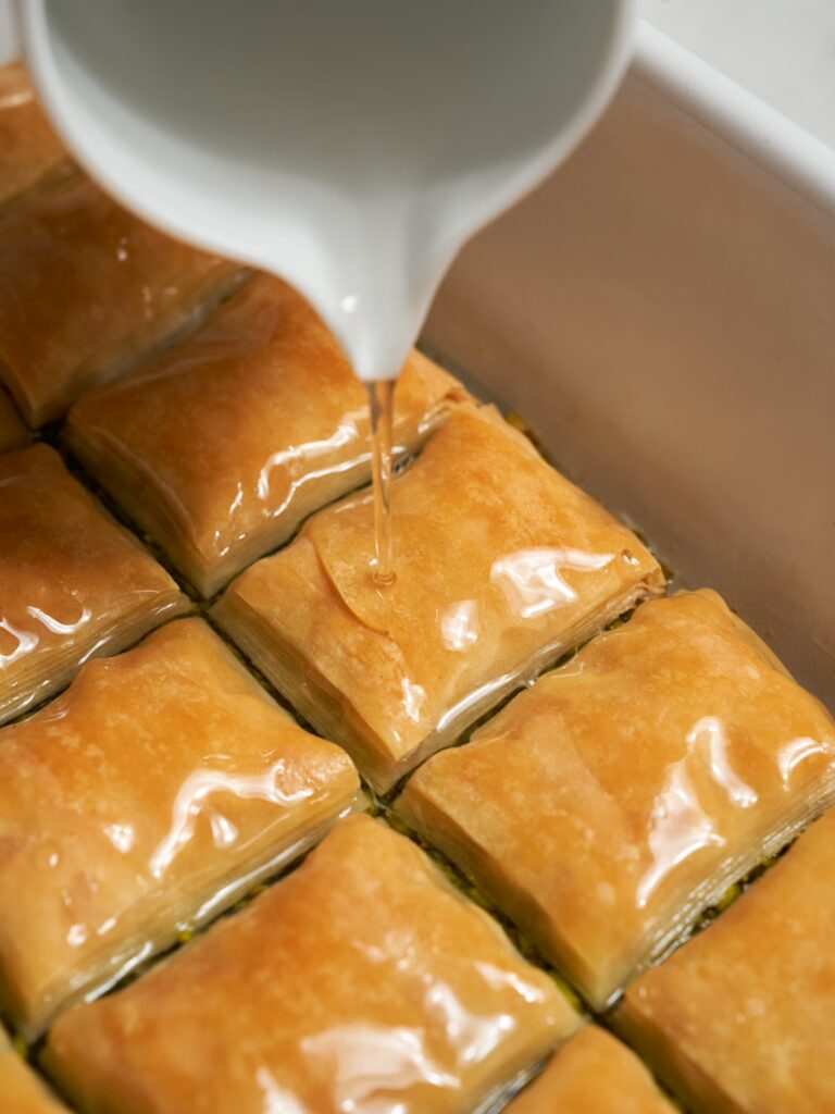 Gebackenes Pistazien Baklava wird mit heißem Zuckersirup übergossen.