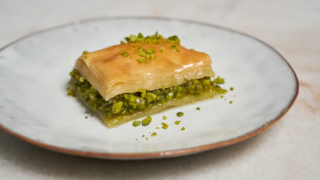 Ein Stück Baklava mit Pistazien auf einem kleinen Teller.
