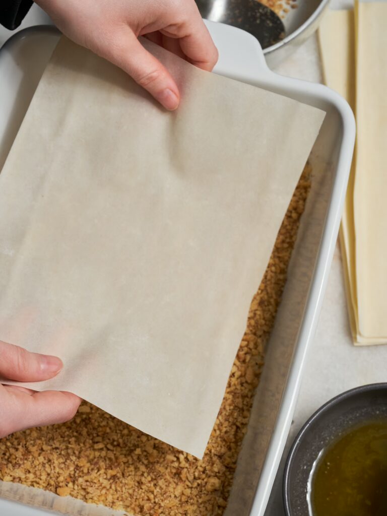 Ein Blatt Filoteig wird auf die Walnuss Füllung für das Baklava gelegt.