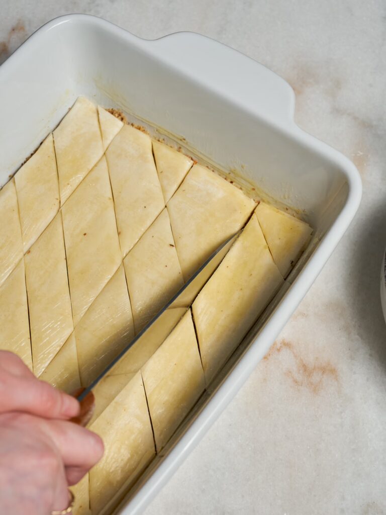 Das Baklava mit Walnüssen wird mit einem Messer in Rauten geschnitten.