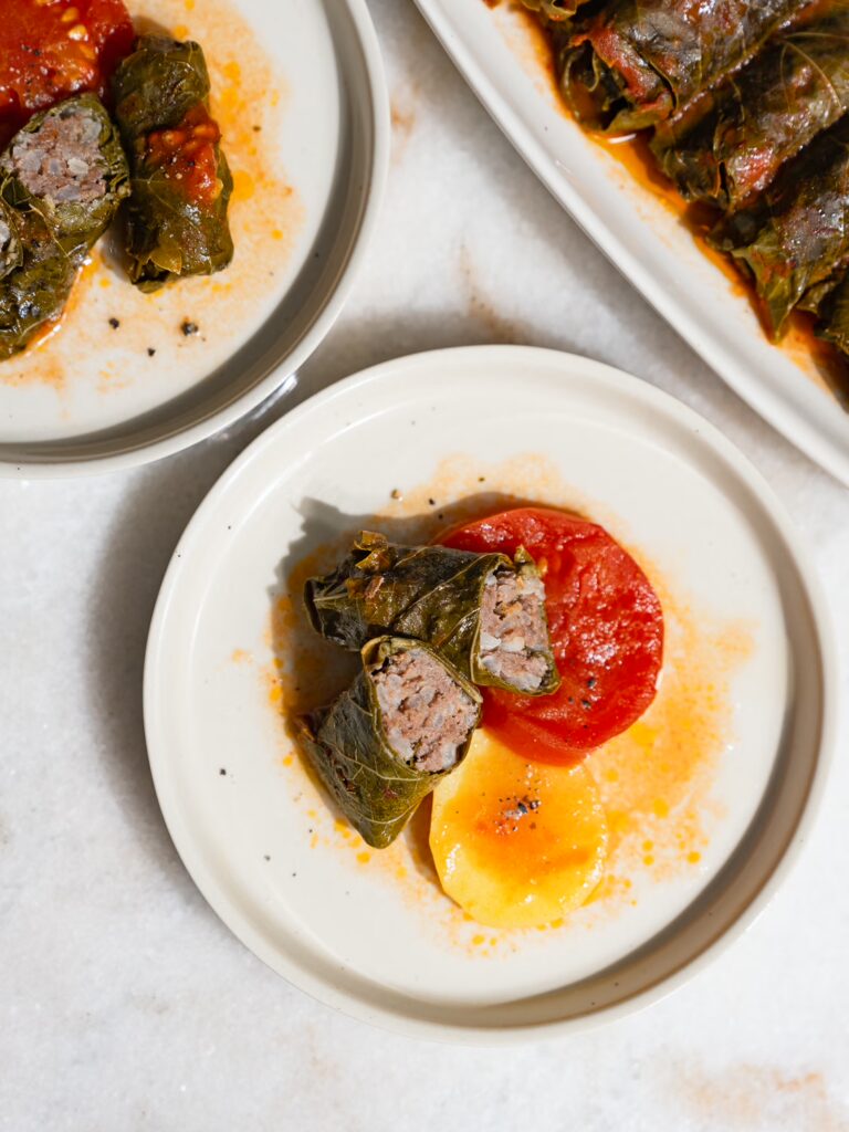 Stuffed grape leaves with minced meat cut in half on a small plate and served with potato and tomato.