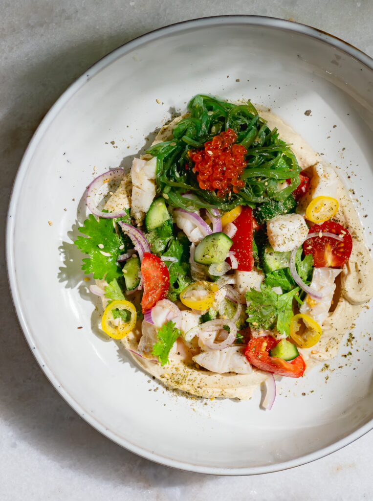 Ceviche auf Hummus angerichtet in einer hellen Schale.