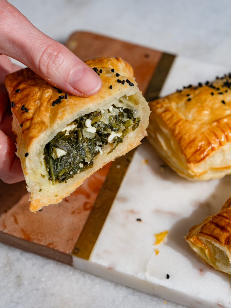 Pâte feuilletée avec des épinards et de la feta cuite en poche et coupée en deux sur une planche.
