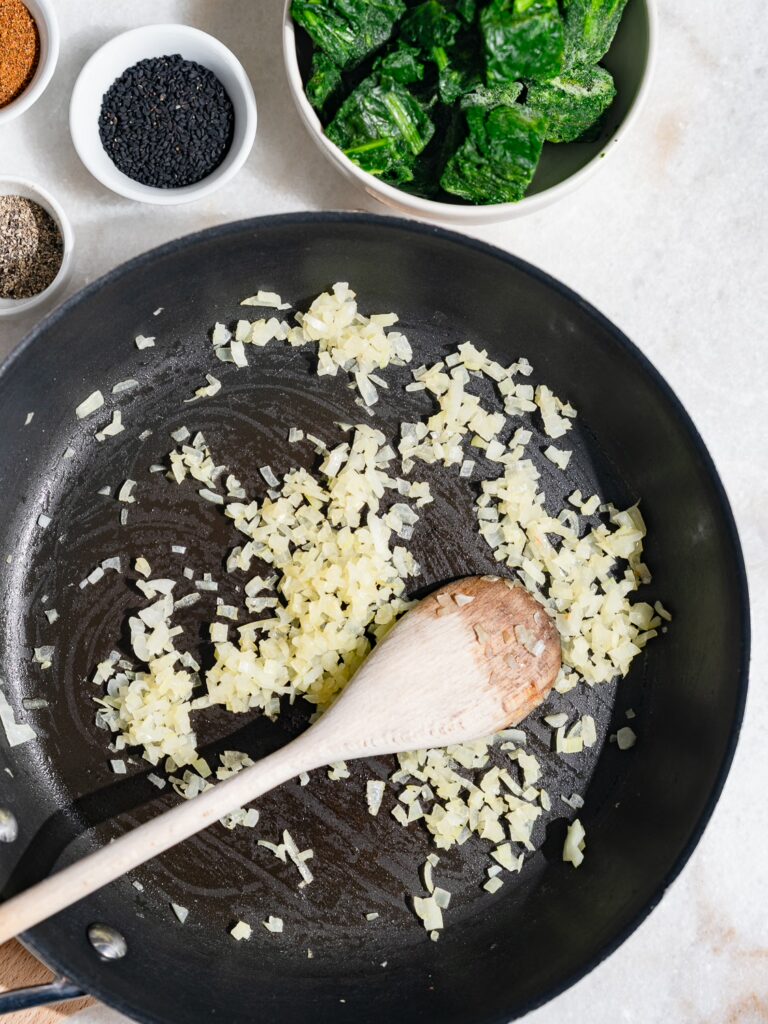 Les dés d'oignons sont sautés dans une poêle pour les feuilletés aux épinards et à la feta.