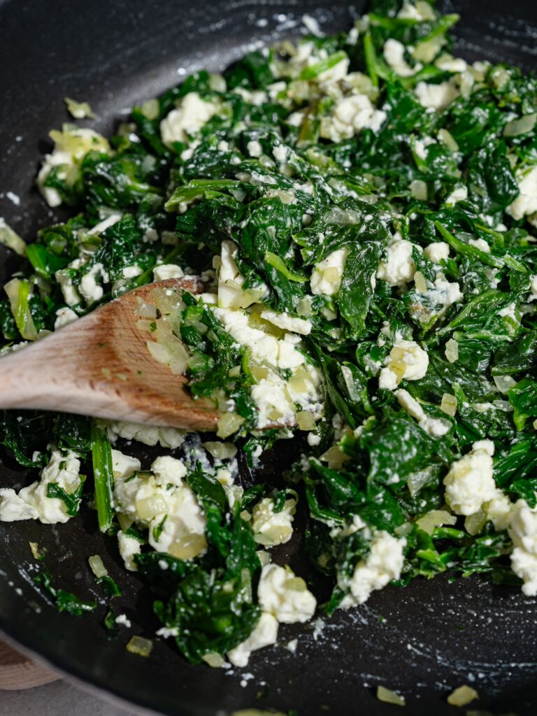 Le mélange d'épinards et de feta est mélangé dans une poêle pour la pâte feuilletée.