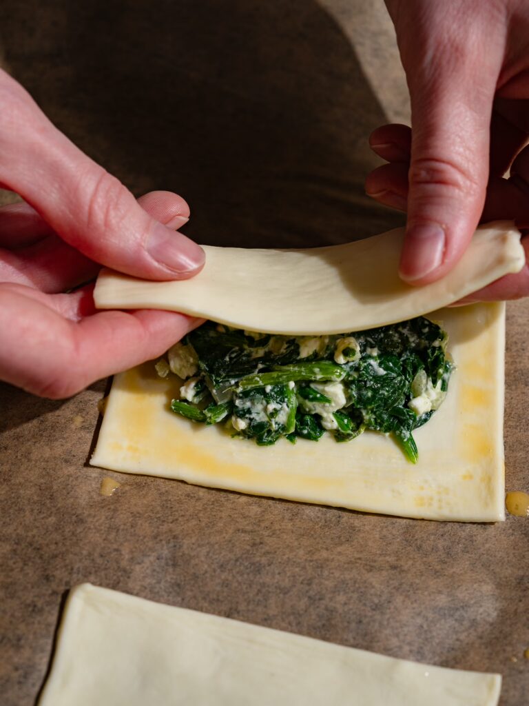La pâte feuilletée est assemblée pour former un chausson de pâte feuilletée aux épinards et à la feta.